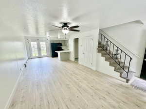 Unfurnished living room with a textured ceiling, light wood finished floors, a ceiling fan, a baseboard radiator, and french doors