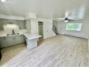 Kitchen with a textured ceiling, light countertops, gray cabinetry, a baseboard radiator, and light wood-type flooring