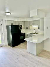 Kitchen with light countertops, a peninsula, black appliances, a textured ceiling, and light wood finished floors