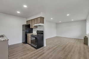 Kitchen featuring black appliances, light wood finished floors, recessed lighting, light countertops, and open floor plan