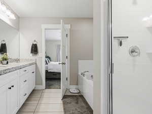 Ensuite bathroom featuring a walk in closet, double vanity, a shower stall, garden tub, granite countertop and light tile floors