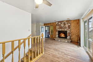 Unfurnished living room featuring wooden walls, a fireplace, light wood-type flooring, and ceiling fan