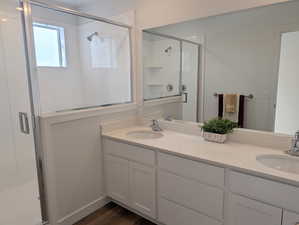 Full bath with a shower stall, double vanity, and dark wood-style flooring