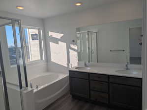 Bathroom with double vanity, a garden tub, a shower stall, dark wood-style flooring, and recessed lighting