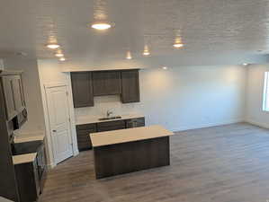 Kitchen with a textured ceiling, a center island, dark wood-type flooring, dark wood finish cabinetry, and stainless steel appliances