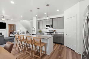 Kitchen featuring gray cabinets, open floor plan, a breakfast bar area, light stone countertops, and an island with sink