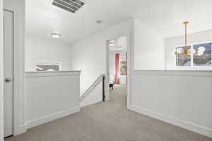 Hallway featuring an upstairs landing, light carpet, and hanging lights