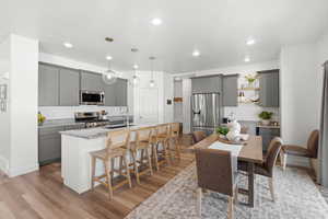 Kitchen with gray cabinetry, light stone countertops, stainless steel appliances, and light wood finished floors