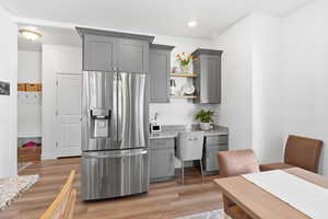Kitchen featuring gray cabinets, stainless steel fridge with ice dispenser, light stone counters, light wood-type flooring, and open shelves