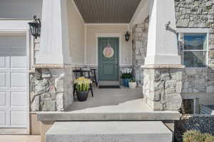 Doorway to property with stone siding, a porch, and a garage