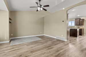 Unfurnished living room featuring a ceiling fan, arched walkways, light wood-style flooring, lofted ceiling, and recessed lighting