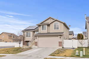 View of front of house with a gate, brick siding, driveway, roof mounted solar panels, and an attached garage