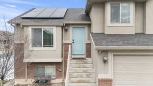 Property entrance featuring stucco siding, a garage, brick siding, and roof with shingles