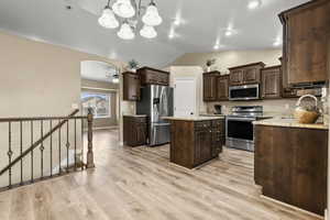 Kitchen featuring dark wood finish cabinets, stainless steel appliances, vaulted ceiling, a center island, and light stone counters