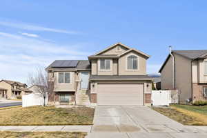 View of front of house featuring a gate, brick siding, concrete driveway, roof mounted solar panels, and stucco siding