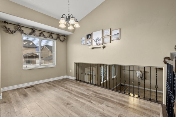 Empty room with vaulted ceiling, suspended lighting, and light wood-style flooring