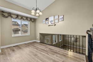 Empty room with vaulted ceiling, suspended lighting, and light wood-style flooring
