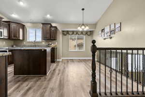 Kitchen with dark wood finish cabinetry, hanging lights, a center island, vaulted ceiling, and light wood-type flooring
