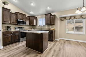 Kitchen featuring dark wood finish cabinetry, stainless steel appliances, a kitchen island, light wood-type flooring, and vaulted ceiling