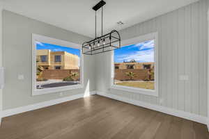 Unfurnished dining area with suspended lighting, hardwood / wood-style flooring, and wooden walls