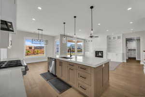 Kitchen featuring a glass covered fireplace, an island with sink, light wood-style floors, and pendant lighting