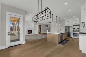 Two tone kitchen featuring two tone cabinetry, a warm lit fireplace, open floor plan, an island with sink, and stainless steel appliances