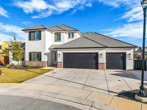 Traditional-style home featuring brick siding, an attached garage, driveway, stucco siding, and a tile roof