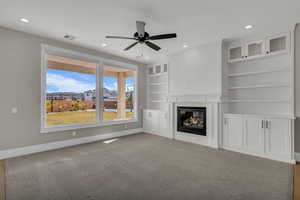 Unfurnished living room with built in shelves, light carpet, ceiling fan, a glass covered fireplace, and recessed lighting