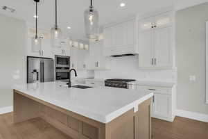 Kitchen with glass insert cabinets, a large island, stainless steel appliances, light wood-style flooring, and light stone countertops