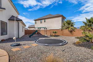 Back of house featuring a trampoline, a playground, stucco siding, and a fenced backyard