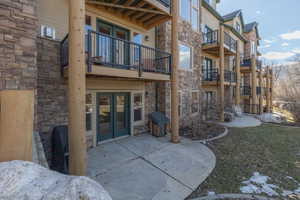 Rear view of property with stone siding, a patio area, a balcony, and french doors