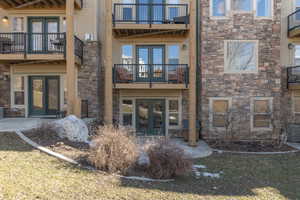 Back of condo with french doors, stone siding, balcony and a patio