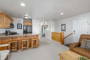 Kitchen featuring a breakfast bar, a peninsula, black appliances, light carpet, and light stone counters