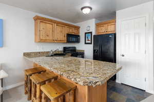 Kitchen with black appliances, a peninsula, a kitchen breakfast bar, light stone counters,