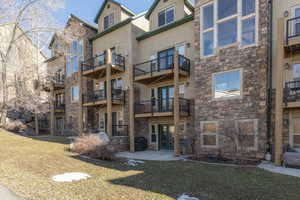 Back of condo with french doors, stone siding, a balcony, and a patio area