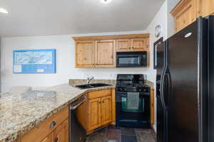 Kitchen featuring black appliances, light stone counters, dark stone finish floors, a breakfast bar