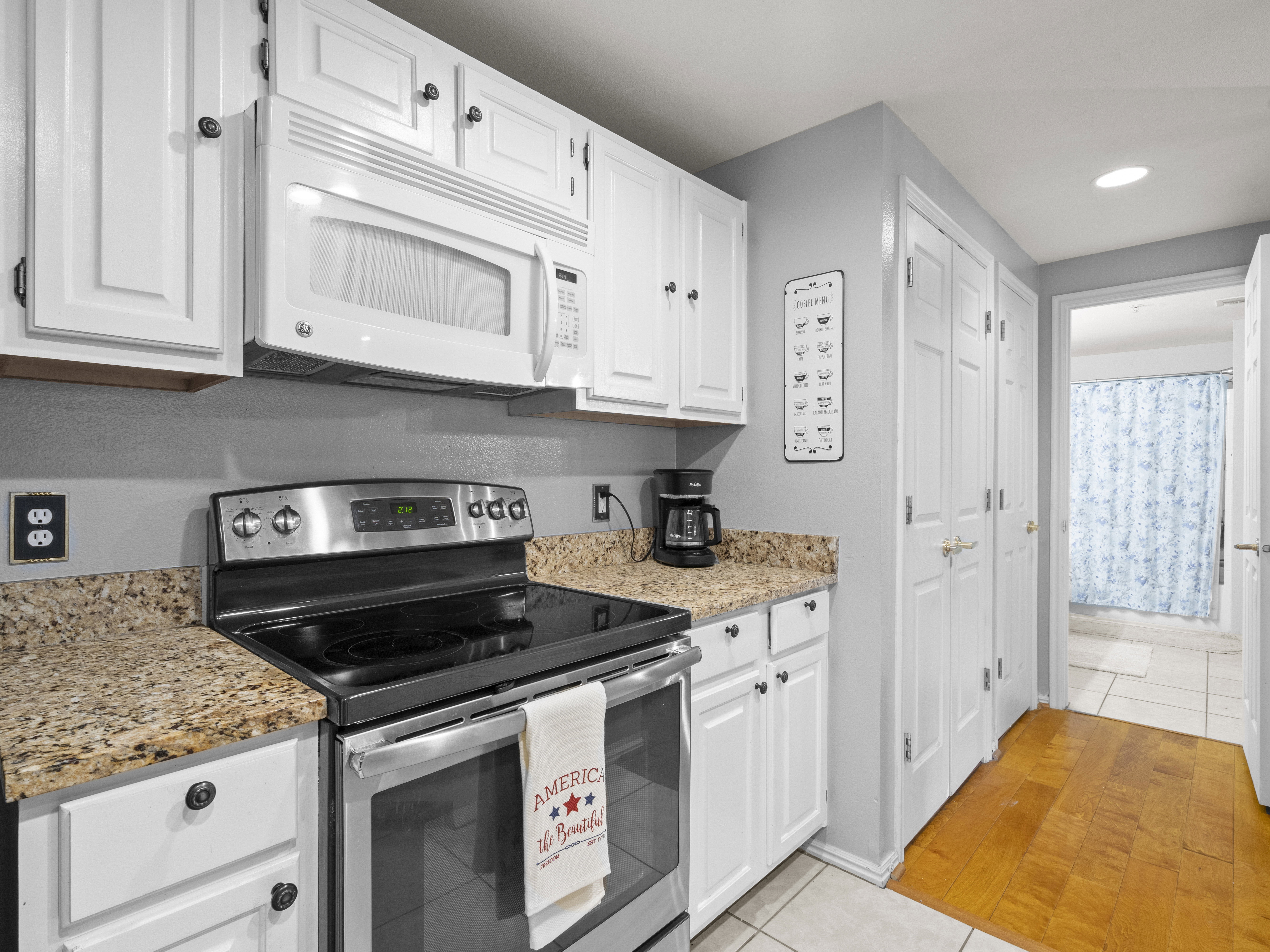 Kitchen featuring stainless steel range with electric stovetop, light tile patterned floors, white microwave, white cabinets, and recessed lighting