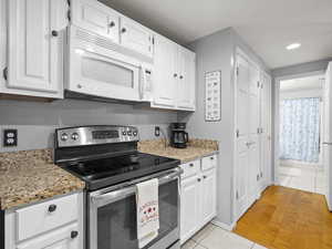 Kitchen featuring stainless steel range with electric stovetop, light tile patterned floors, white microwave, white cabinets, and recessed lighting