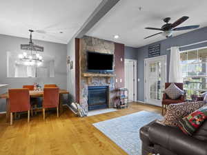Living room with a stone fireplace, light wood-style floors, suspended lighting, and a ceiling fan