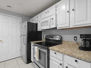 Kitchen featuring stainless steel electric range oven, white microwave, white cabinets, light stone countertops, and light tile patterned floors