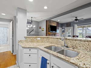 Kitchen with light stone counters, white cabinets, open floor plan, ceiling fan, and light wood-type flooring