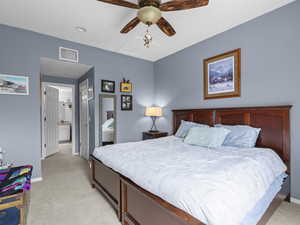 Bedroom with light colored carpet, ensuite bath, and a ceiling fan