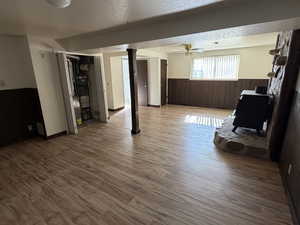 Unfurnished living room with a wainscoted wall, wooden walls, a wood stove, wood finished floors, and strapped water heater