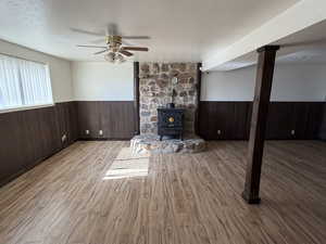 Unfurnished living room with a wainscoted wall, wooden walls, a wood stove, light wood-style flooring, and a textured ceiling