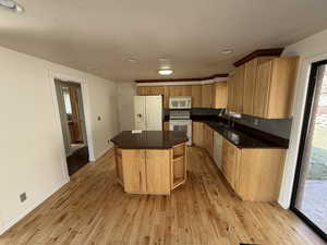 Kitchen featuring white appliances, a kitchen island, light wood-style floors, recessed lighting, and dark stone countertops