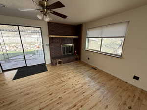 Unfurnished living room featuring a fireplace, ceiling fan, and light wood finished floors