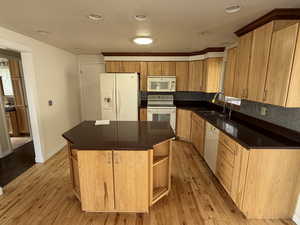 Kitchen featuring white appliances, a kitchen island, open shelves, light wood finished floors, and recessed lighting