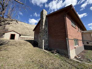 View of side of home featuring brick siding, a chimney, a yard, and a storage unit