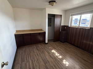 Unfurnished dining area featuring a wainscoted wall, dark wood-type flooring, wooden walls, a textured ceiling, and electric panel
