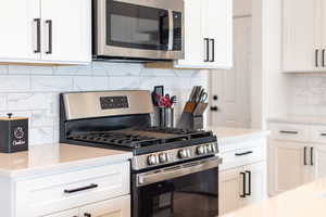 Kitchen with stainless steel appliances, tasteful backsplash, white cabinets, and light stone countertops